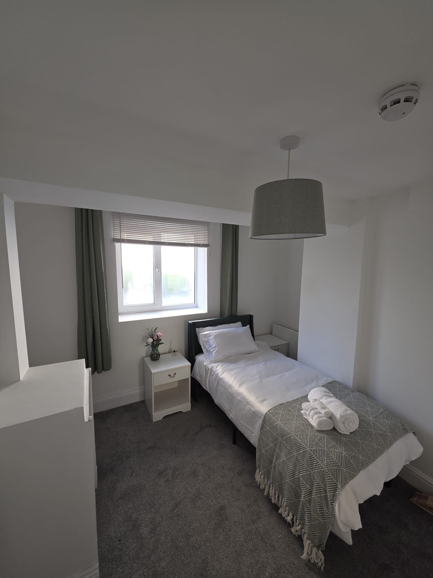 Single bedroom with green curtains and bedside flowers