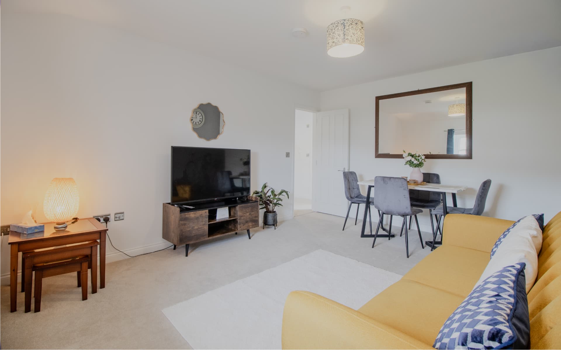 Open-plan lounge with mustard sofa, dining table and smart TV