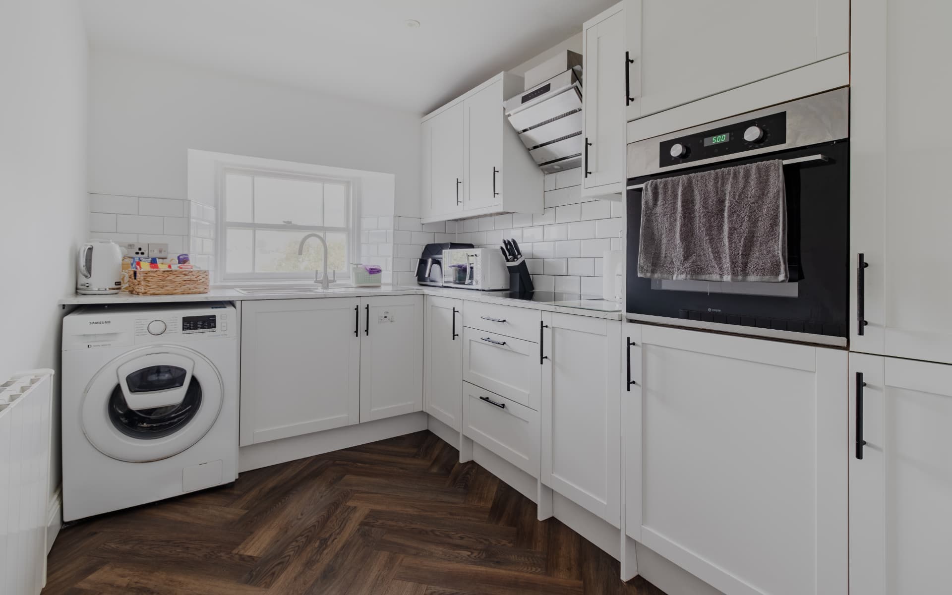 White shaker kitchen with herringbone floor, oven and washing machine